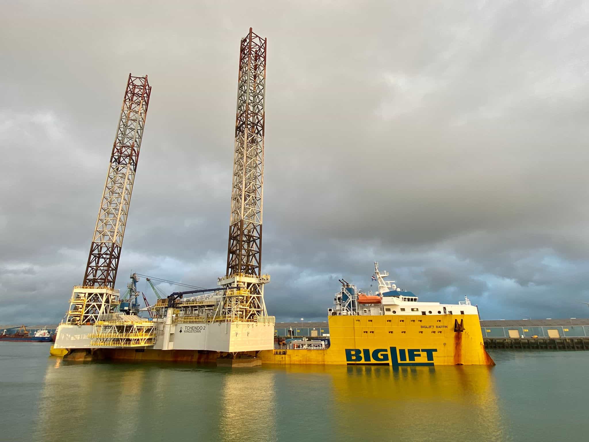 Offshore vessel by pier under cloudy sky.
